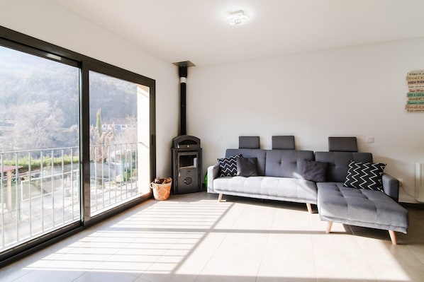 A modern living room with a sofa, a fireplace, and a large window overlooking a balcony.