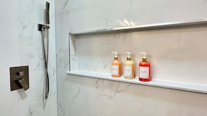 Kylpyhuone, jossa on suihku, hylly, jossa on kolme pulloa hygieniatuotteita, ja marmoriseinä.