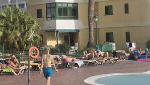 Ein mehrstöckiges Gebäude mit Balkonen, einer Palme und einem Poolbereich mit Liegestühlen.