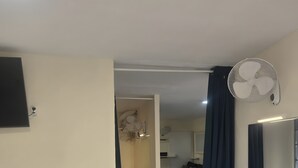 Ein Hotelzimmer mit einem Bett, einem Schminktisch, einem Spiegel, einem Ventilator und einem an der Wand befestigten Fernseher.