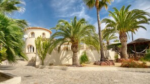 Un patio con palmeras, un edificio con ventanales de arco y un área empaveda de piedra.