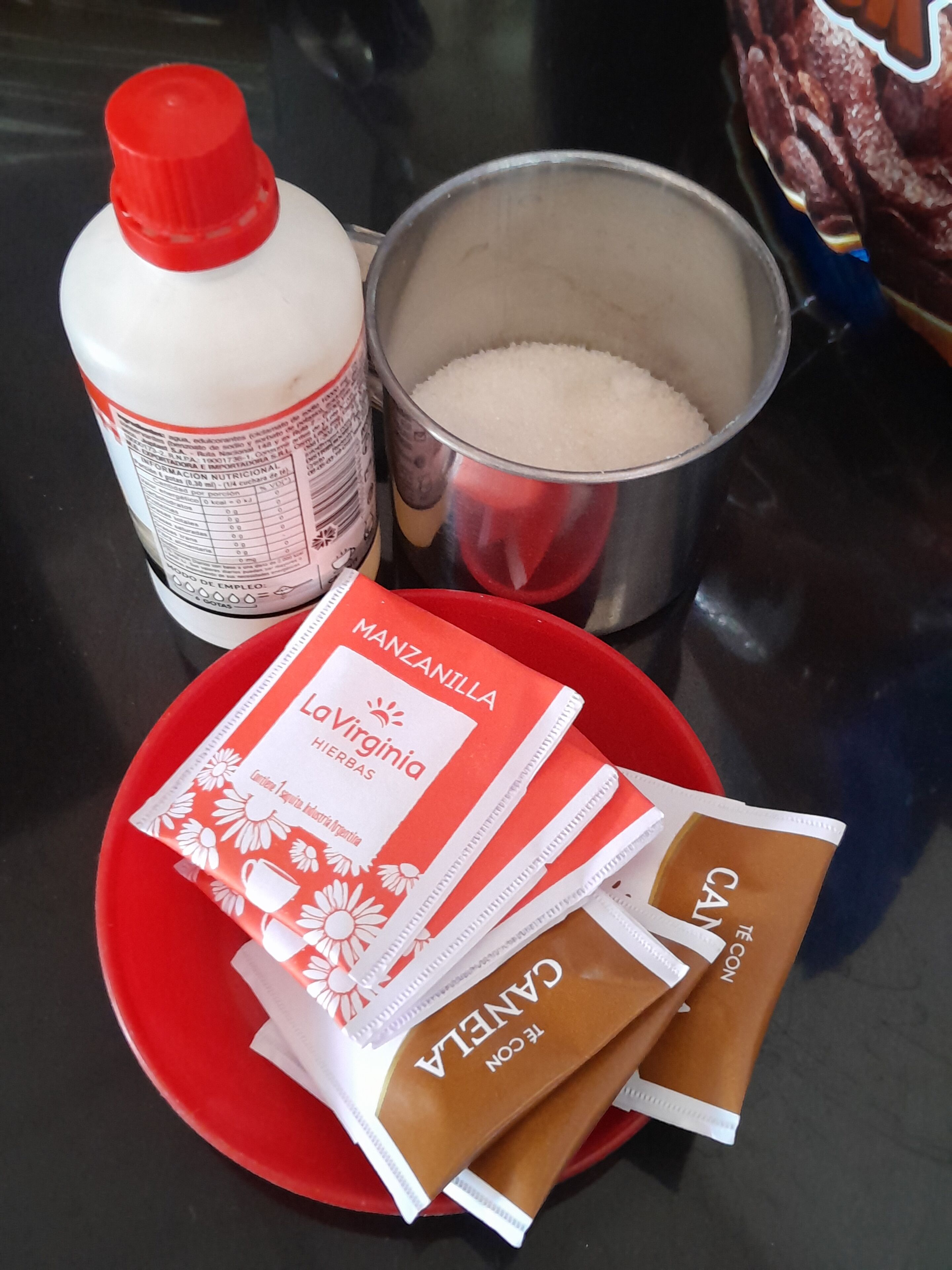 Ein Tisch mit einem roten Teller, der Teebeutel, eine Flasche und einen Zuckerbehälter enthält.