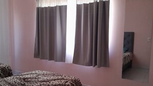 Ein Schlafzimmer mit Bett, einem Fenster mit Vorhängen, einem Spiegel und einem Fliesenboden.