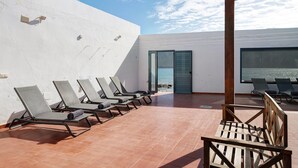 Eine Terrasse mit Liegestühlen, einer Holzbank und Blick auf das Meer.