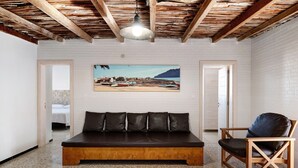 Ein Zimmer mit Holzbalkendecke, einem großen Bett, einem Sessel und einem an der Wand hängenden Bild.