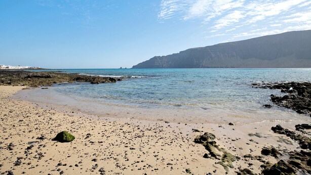 Ein Strand mit blauem Himmel, felsigem Ufer und fernen Klippen.