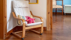 A wooden rocking chair with a cushioned seat and back, positioned in a corner with a tiled floor and a wooden door frame.