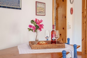 Una mesa de comedor con una bandeja de mimbre, un florero con flores rosadas, dos copas de vino y una botella de vino tinto.