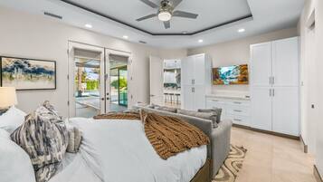 A modern bedroom with a bed, a ceiling fan, and a view of the kitchen through an open door.