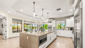 A modern kitchen with a large island, white cabinetry, stainless steel appliances, and pendant lighting. - Cinema+Golf S’m+P P’g +Volley+Basket+Pickle+G’room (Bermuda Dunes)