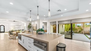 A spacious kitchen with a large island, modern pendant lights, and a view to an outdoor patio. - Cinema+Golf S’m+P P’g +Volley+Basket+Pickle+G’room (Bermuda Dunes)
