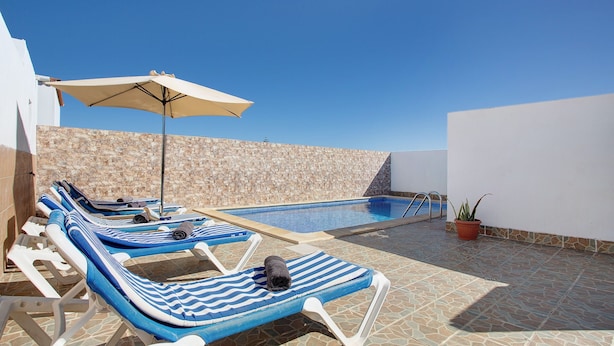 Un área junto a la piscina con sillones de descanso, piscina y un muro de piedra.