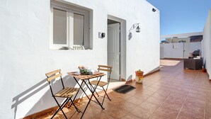 Un edificio blanco con ventana, puerta, una mesa con sillas y una planta en maceta.