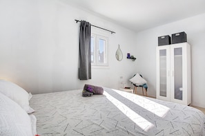 A bedroom with a bed, a wardrobe, a window with curtains, a bedside table, and a hanging mirror.