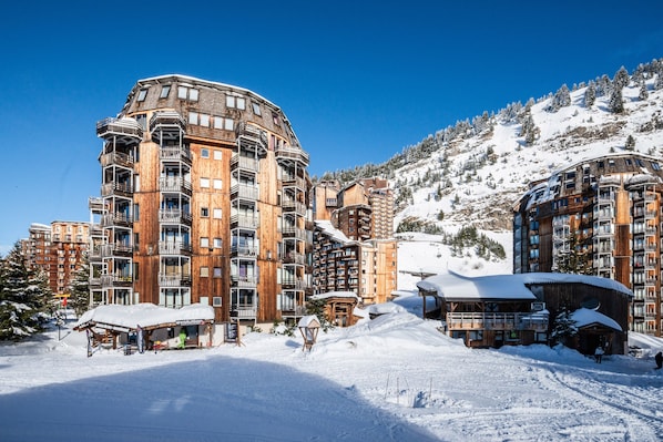 Un hôtel à plusieurs étages doté de balcons, avec une piste de ski en arrière-plan et un paysage enneigé.
