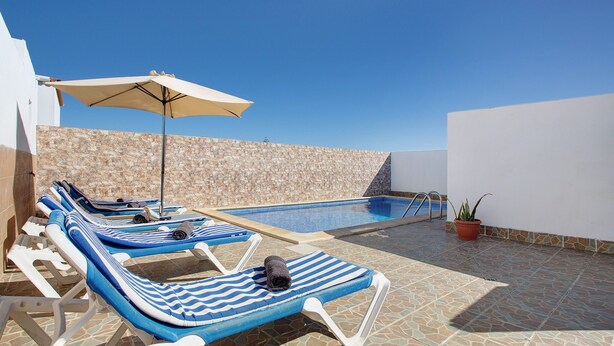 Uma área à beira da piscina com espreguiçadeiras, piscina e uma parede de pedra.
