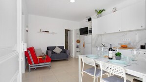 Uma cozinha moderna com armários brancos, uma mesa de jantar com cadeiras, um sofá vermelho e uma TV fixada acima do balcão.