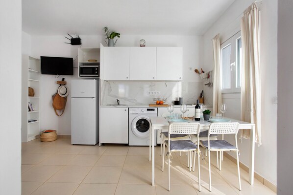 A compact kitchen with a washing machine, microwave, and dining area with chairs and a table.