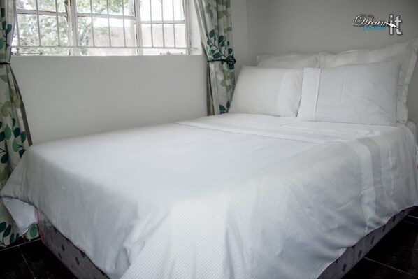 Una cama bien hecha con sábanas blancas en una habitación con ventana y cortinas.