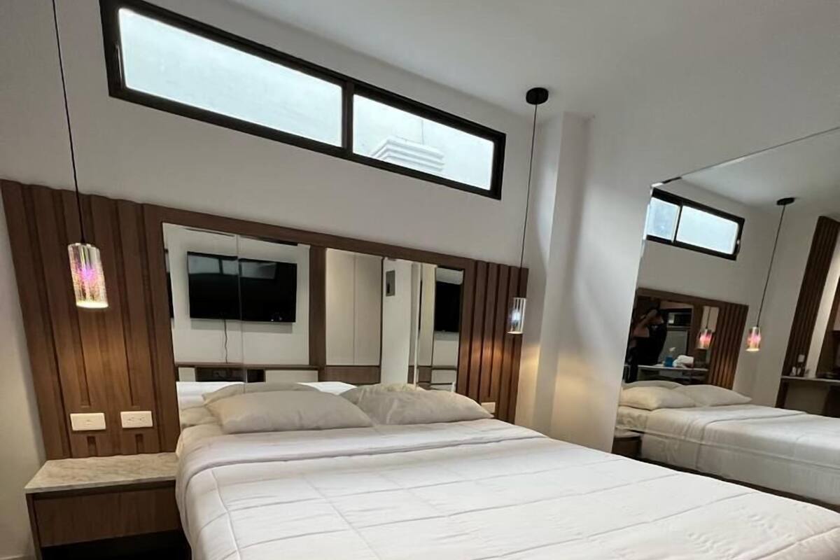 A modern bedroom with a large bed, a TV mounted on the wall, and a window above the bed.