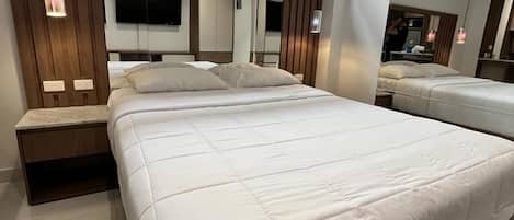 A modern bedroom with a large bed, a TV mounted on the wall, and a window above the bed.