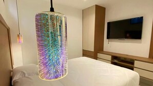 Ein modernes Schlafzimmer mit Bett, Wand-Fernseher und einer einzigartigen, farbenfrohen Pendelleuchte.