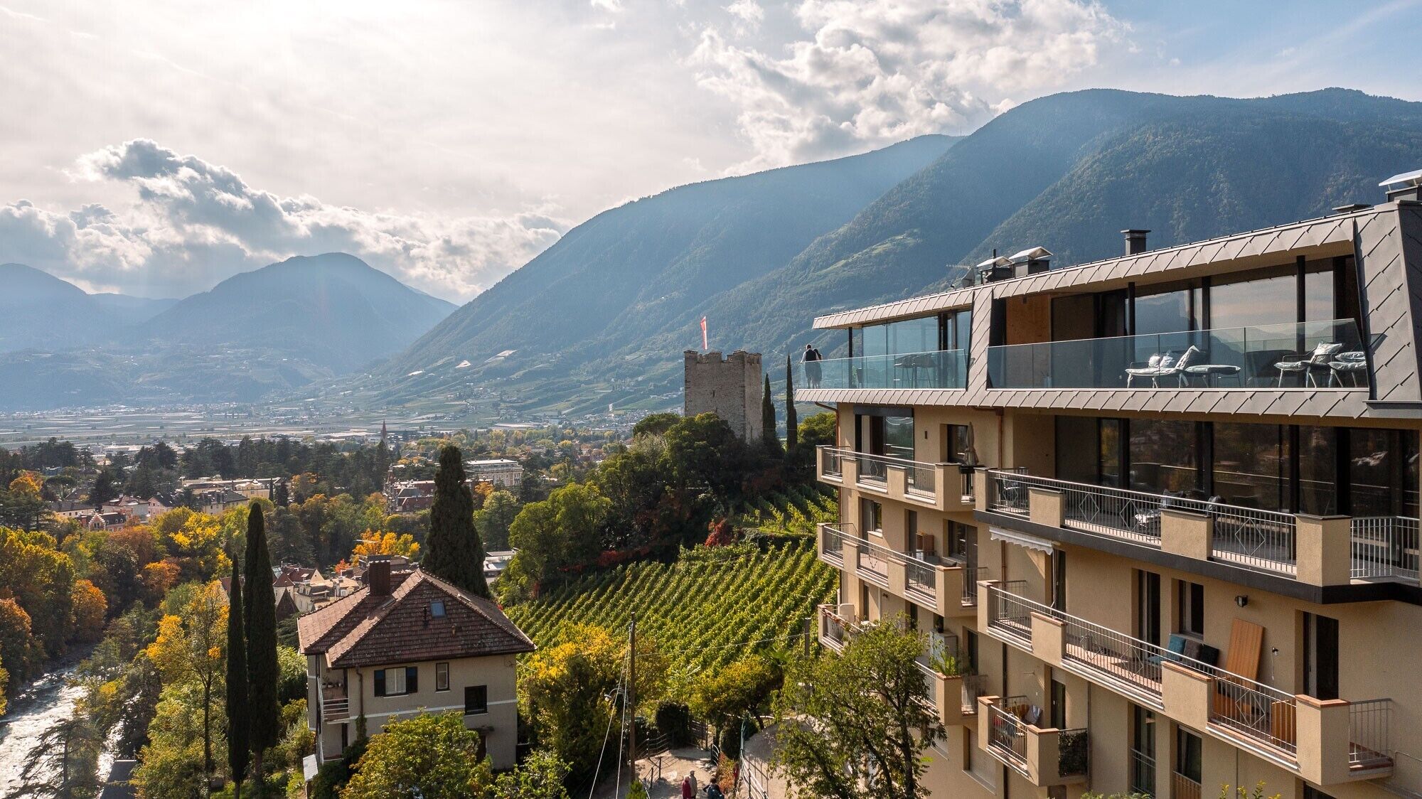 Un bâtiment moderne doté de balcons, un vignoble et des montagnes en arrière-plan.