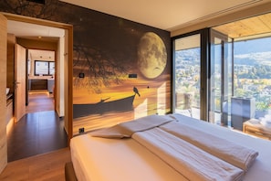 Quarto com cama grande, vista para a cidade e um mural com a lua e um barco.