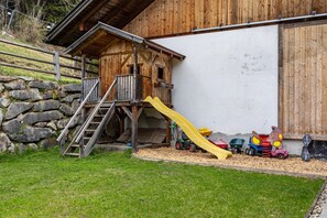 Une cabane en bois avec un toboggan, un mur en pierre et une zone herbeuse.