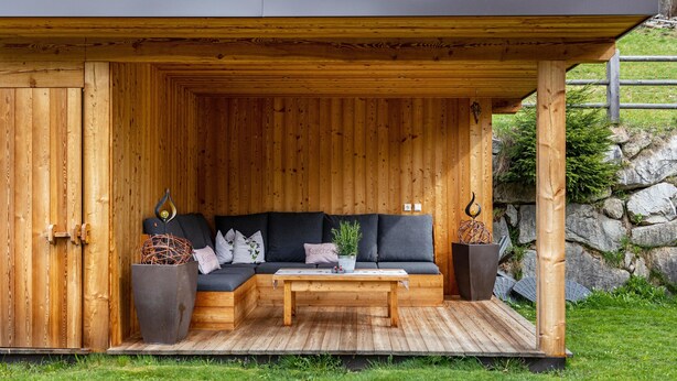 A wooden cabin with a built-in sofa, a coffee table, and two large planters.