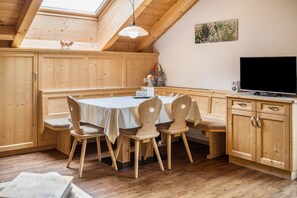 A wooden dining area with a table and chairs, a TV, and a painting on the wall.
