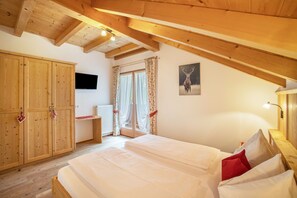 A bedroom with a wooden ceiling, a bed with white bedding, a wooden wardrobe, a television, and a window with curtains.
