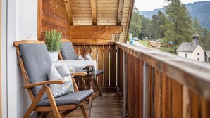 Un balcon en bois avec deux chaises et une table, offrant une vue panoramique sur un paysage magnifique, avec des montagnes et des arbres.
