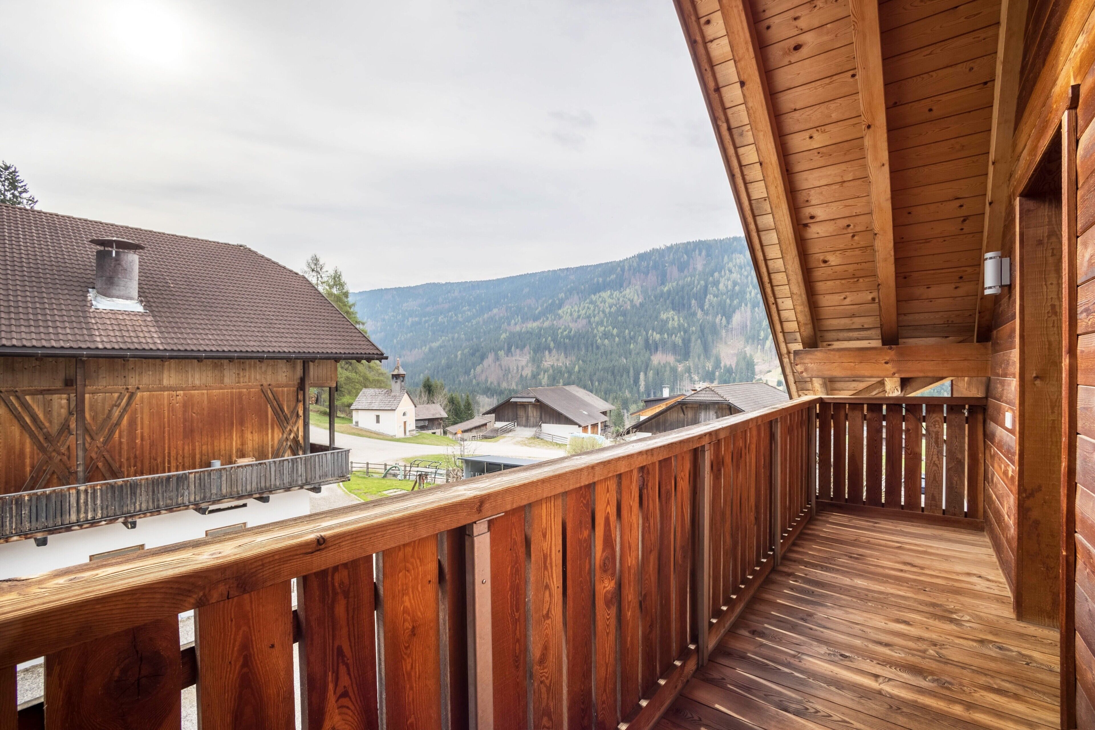 A wooden balcony with a view of houses and mountains.