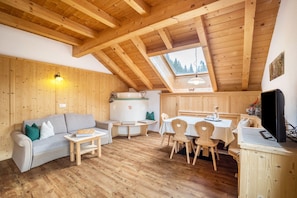 A wooden interior with a lofted ceiling, a sofa, a dining table with chairs, and a television.