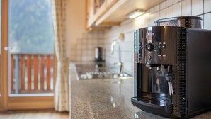 Une machine à café posée sur un plan de travail dans une cuisine, avec une fenêtre et une porte en arrière-plan.