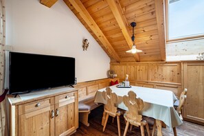 Un intérieur en bois avec un téléviseur posé sur un meuble, une table à manger avec des chaises et un luminaire au plafond.