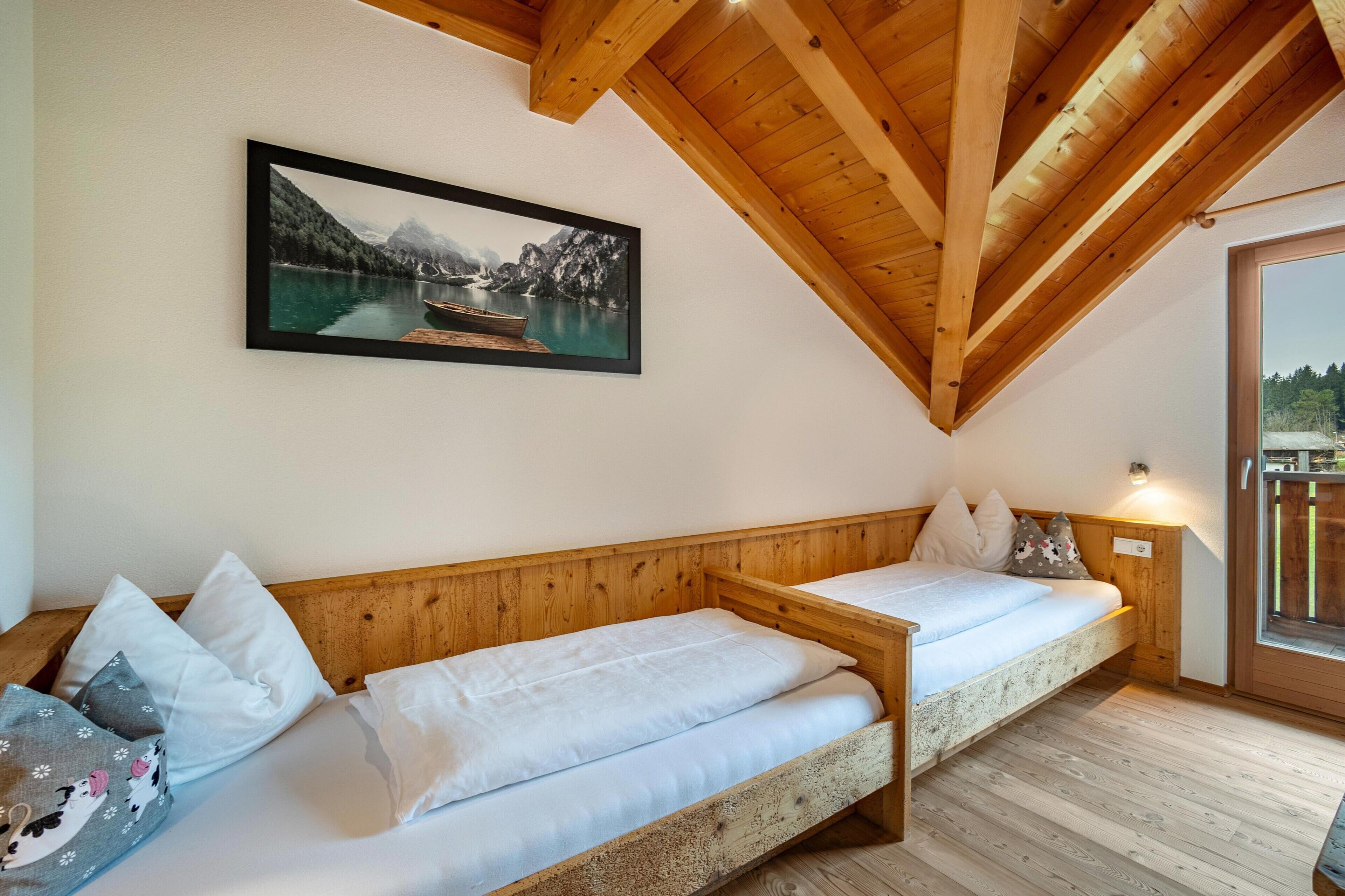 Ein Zimmer mit Holzbalkendecke, einem Bett mit weißer Bettwäsche, einem gerahmten Bild eines Sees und einem Fenster mit Blick.