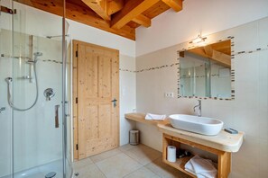 Une salle de bain moderne avec une douche en verre, une porte en bois, un lavabo blanc et un miroir avec un pare-splash en carrelage.