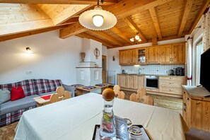 A cozy room with a wooden ceiling, a dining table, a sofa, and a kitchen area.