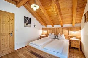 A wooden-paneled bedroom with a bed, bedside tables, a wall-mounted light, and a door.