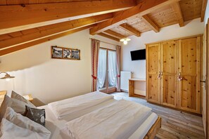Une chambre avec deux lits, des poutres apparentes en bois au plafond, une armoire, un téléviseur et une fenêtre avec des rideaux.