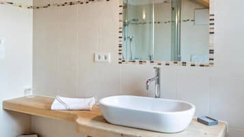 Une salle de bain avec un lavabo blanc, un plan de toilette en bois, un miroir avec un cadre décoratif et une cabine de douche en verre.