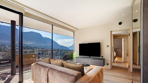 Un salon moderne avec une grande fenêtre, un canapé, un téléviseur et une vue sur les montagnes.