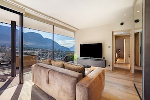 Un salon moderne avec une grande fenêtre, un canapé, un téléviseur et une vue sur les montagnes.