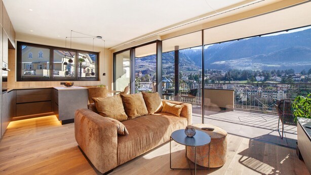Un salon moderne avec un canapé, une table basse et une vue sur le paysage urbain, grâce à de grandes fenêtres.