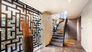 Un intérieur moderne agrémenté d’un escalier, d’un mur décoratif et d’un vase contenant des plantes séchées.