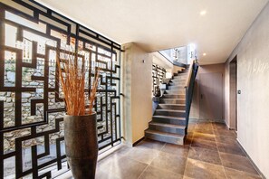 Un intérieur moderne agrémenté d’un escalier, d’un mur décoratif et d’un vase contenant des plantes séchées.