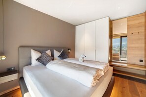 Une chambre moderne avec un grand lit, une table de chevet, une lampe fixée au mur et une vue sur la ville par une fenêtre.