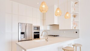Eine moderne Küche mit weißen Schränken, einem Edelstahlkühlschrank, einem eingebauten Backofen, einer Mikrowelle, einem Spülbecken und drei Holzhockern.